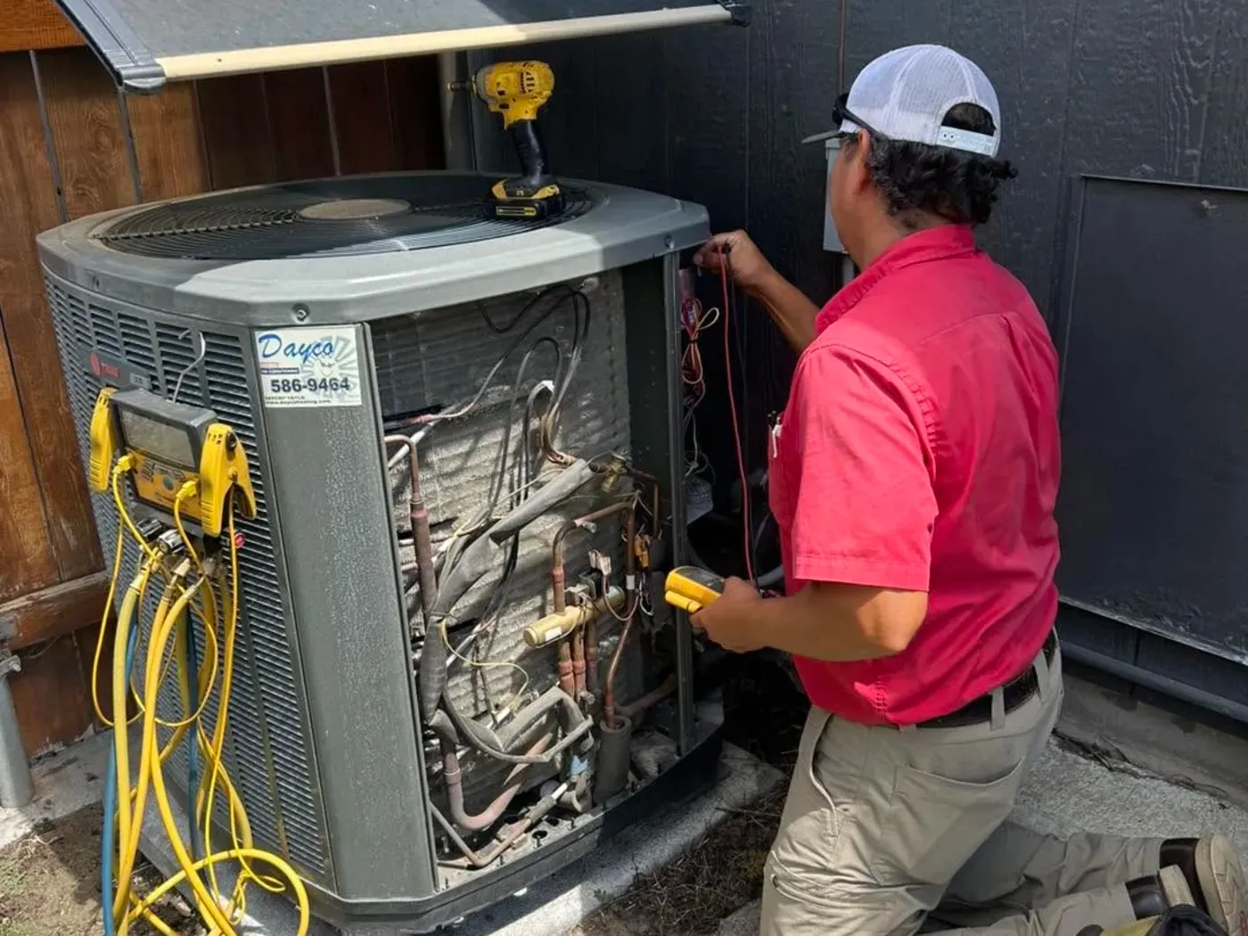 A Dayco technician servicing an outdoor Trane unit beside a house