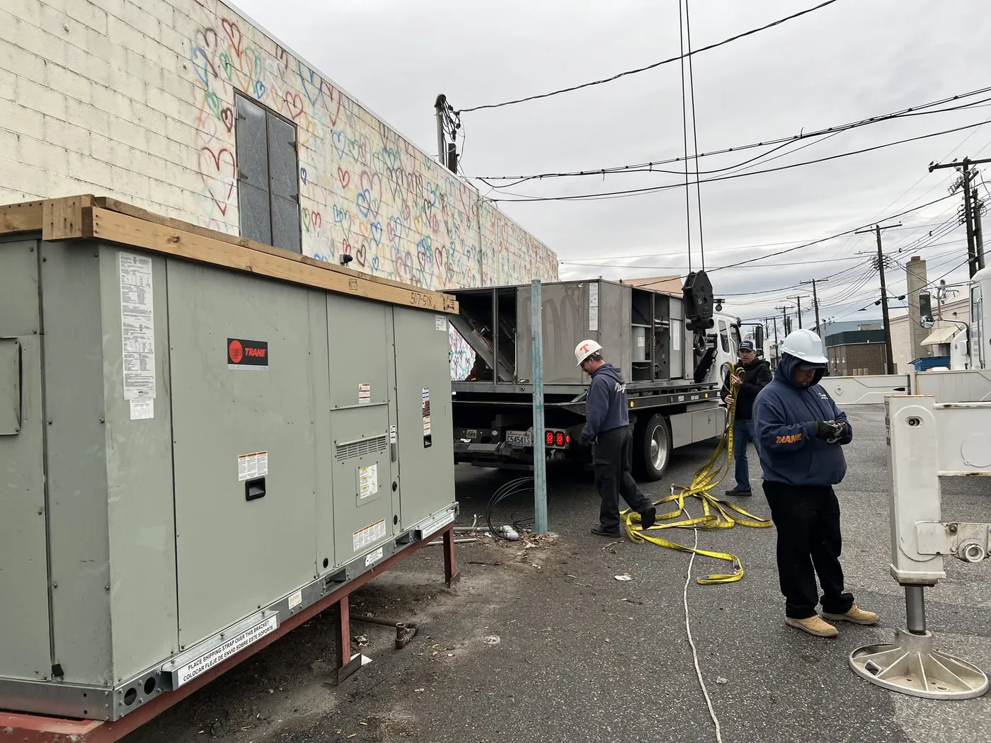 New Trane packaged rooftop units staged in an alley beside a commercial building, with Dayco crew members in hard hats working beside them
