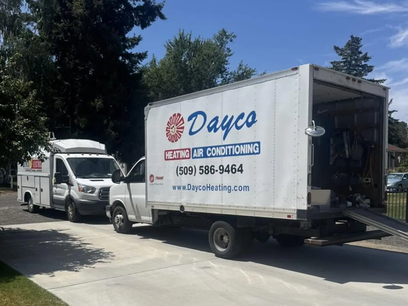 A white Dayco box truck with the red sun logo parked on a residential street beside a Dayco pickup