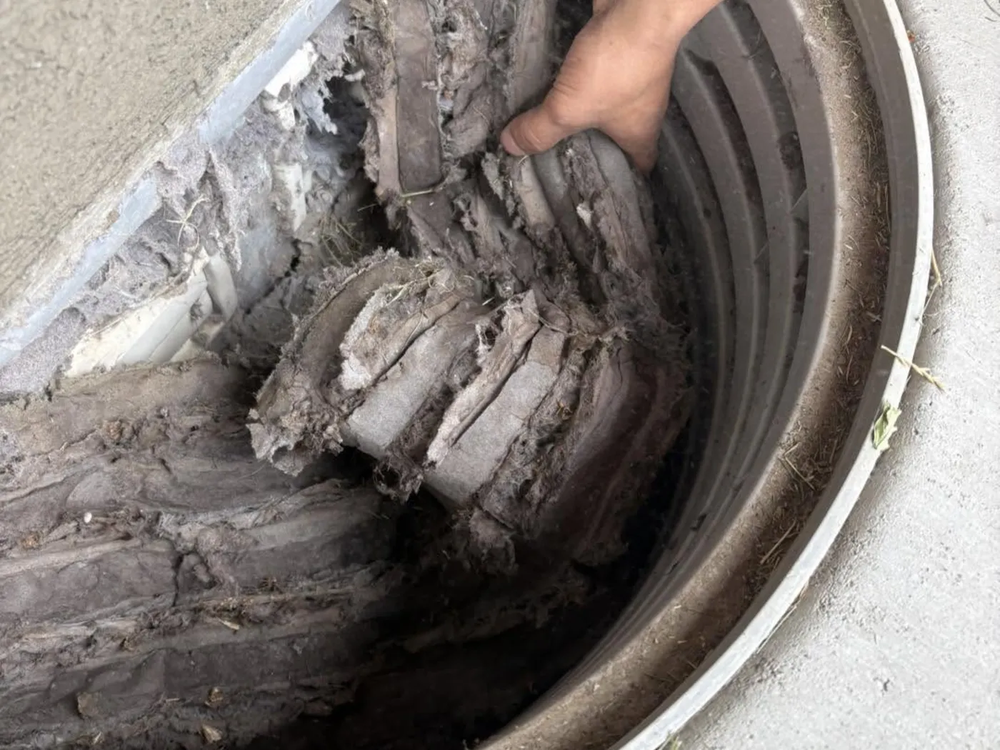 A gloved hand pulling a thick mat of dust out of a residential air duct