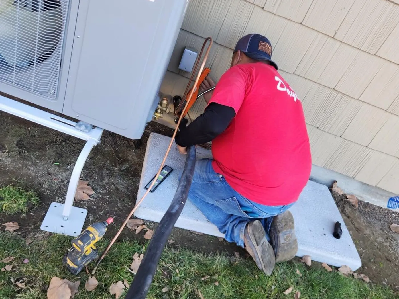 A Dayco technician kneeling to connect a ductless mini-split outdoor unit beside a house