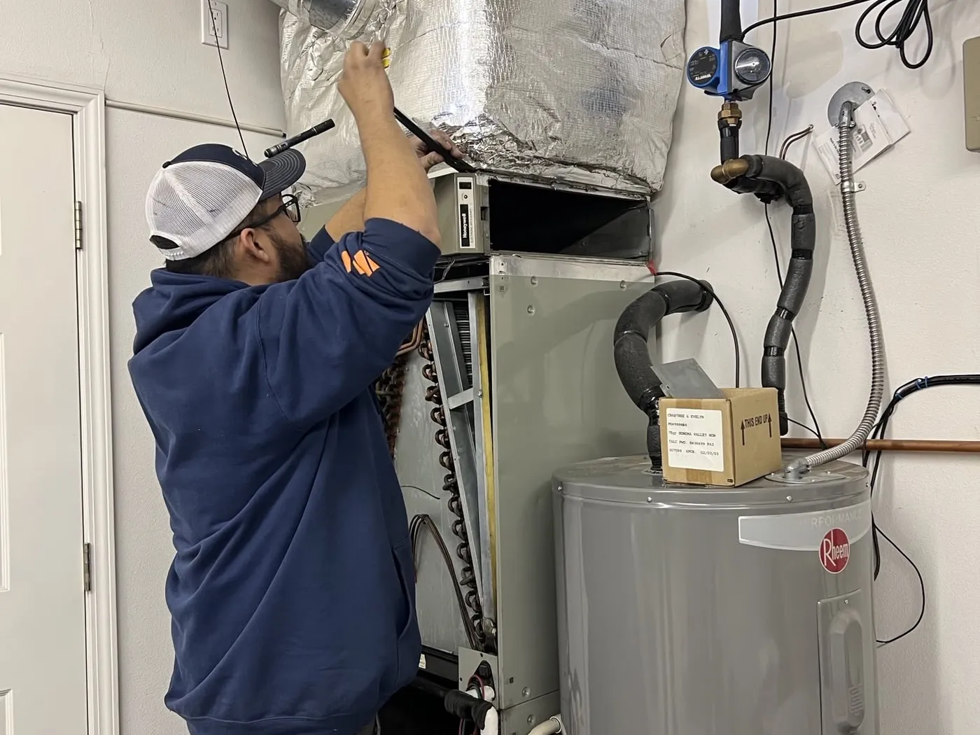 A Dayco technician working on an indoor furnace and duct connection in a utility room